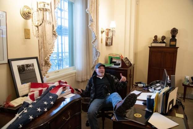 تصویر یکی از هواداران دونالد ترامپ که وارد ساختمان کنگره شده و بر صندلی نانسی پلوس، رئیس دمکرات مجلس نمایندگان نشسته است. (منبعbbc) 